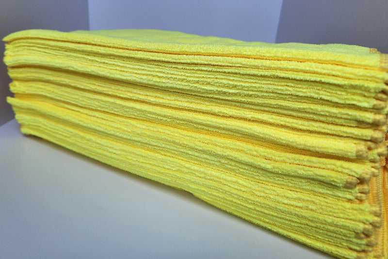 Stack of yellow microfiber cloths on a white surface with a gray background